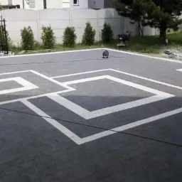 Ułożona, grafitowa kostka brukowa z białymi, geometrycznymi wzorami na podjeździe, widok z góry, brama w tle.