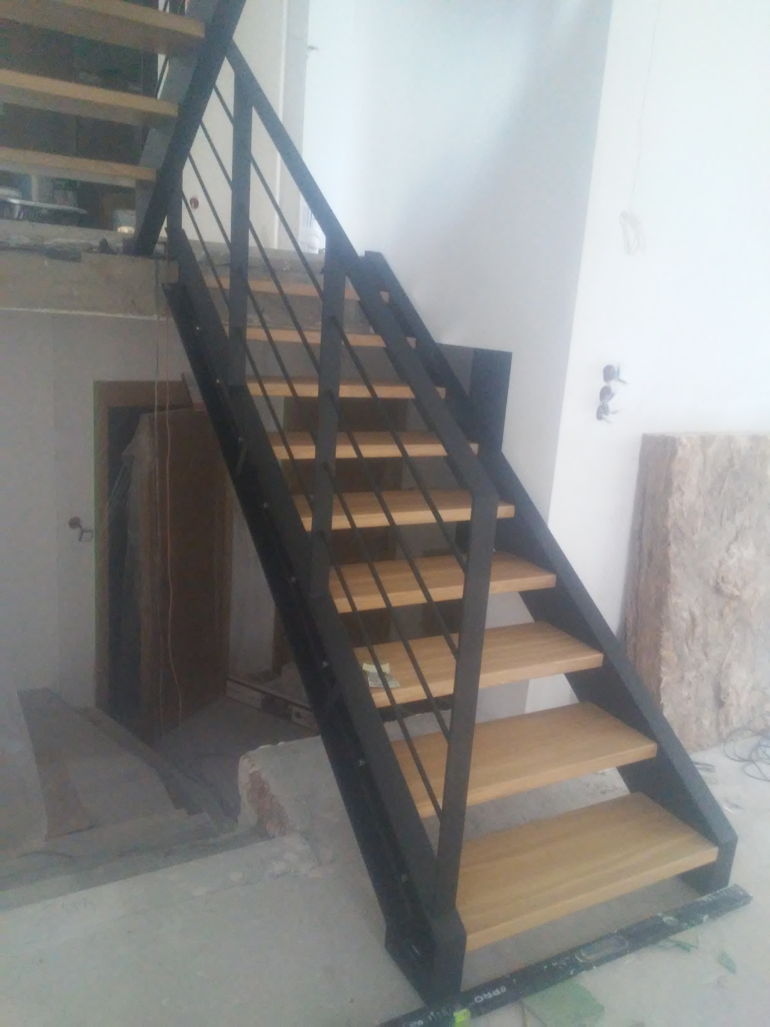 Stalowe schody z drewnianymi stopniami w surowym wnętrzu, widoczne niedokończone ściany i izolacja.