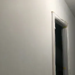 Świeżo pomalowana, jasnoszara ściana z zabezpieczoną folią ościeżnicą, przygotowana do dalszych prac wykończeniowych.