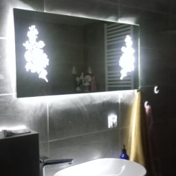 GRZEGORZ NOGA FIRMA HETMAN - Nowoczesna łazienka z umywalką nablatową, podświetlanym lustrem z motywem kwiatowym i szarymi płytkami na ścianach.