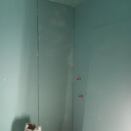 Wnętrze w trakcie montażu płyt kartonowo-gipsowych, widoczny worek z klejem gipsowym i fragment instalacji wodnej z czerwonymi zaślepkami.