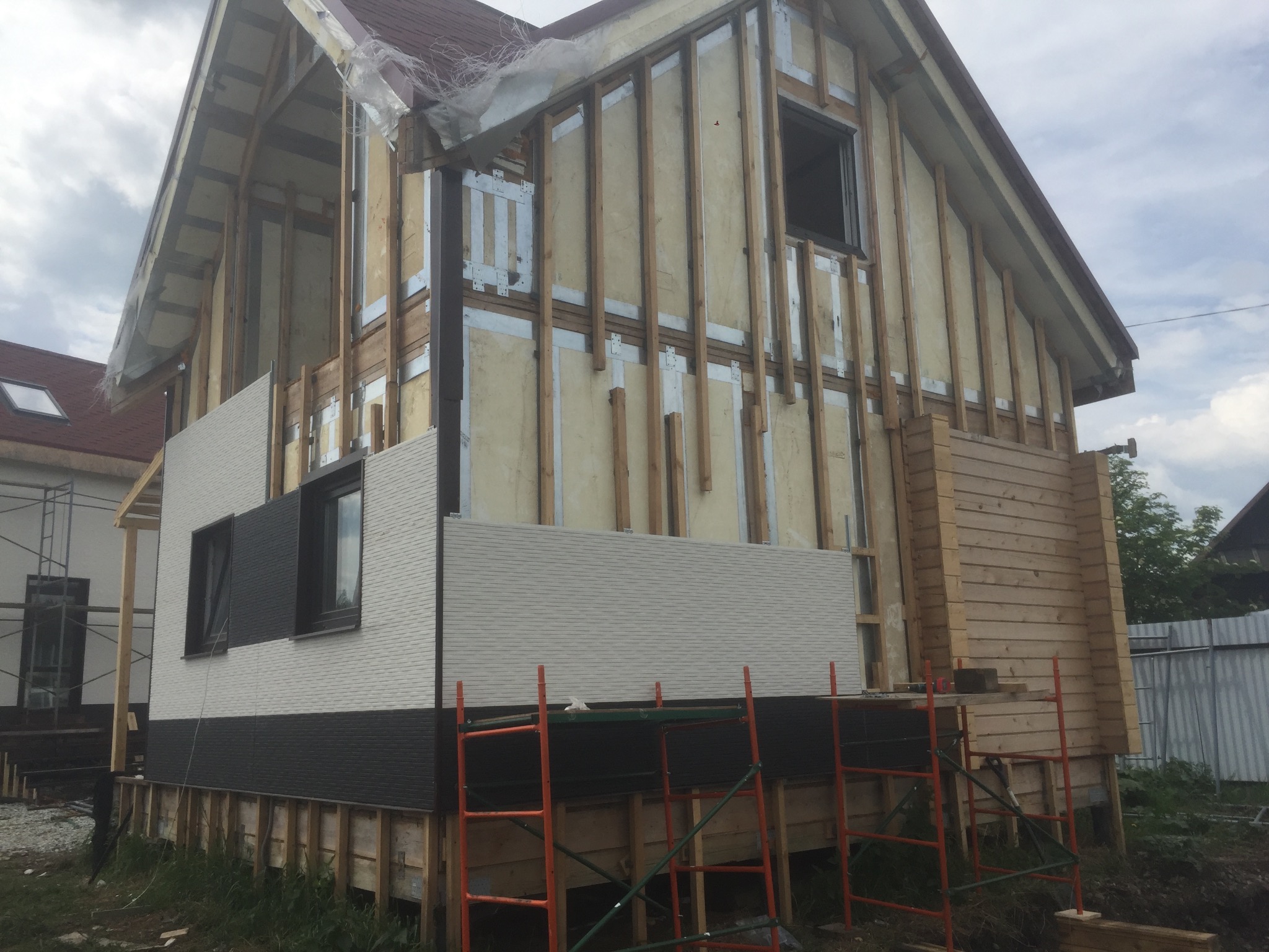 Budowa domu w konstrukcji szkieletowej z częściowo zamontowaną elewacją, widoczne rusztowania i elementy konstrukcyjne.