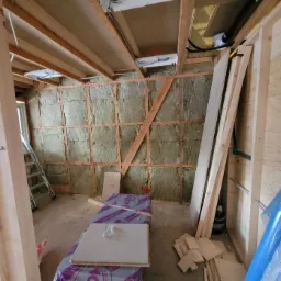 Wnętrze w trakcie ocieplania ścian wełną mineralną w Zamościu, widoczne drewniane legary, płyty kartonowo-gipsowe i drabina.