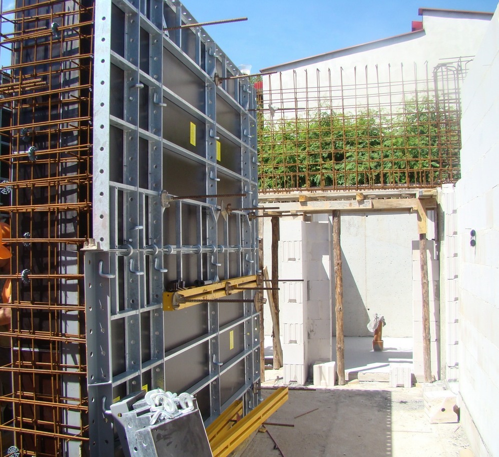 System szalunkowy ENCO36 w trakcie montażu na budowie, widoczne stalowe ramy i zbrojenie, w tle budynek z białego bloczka.