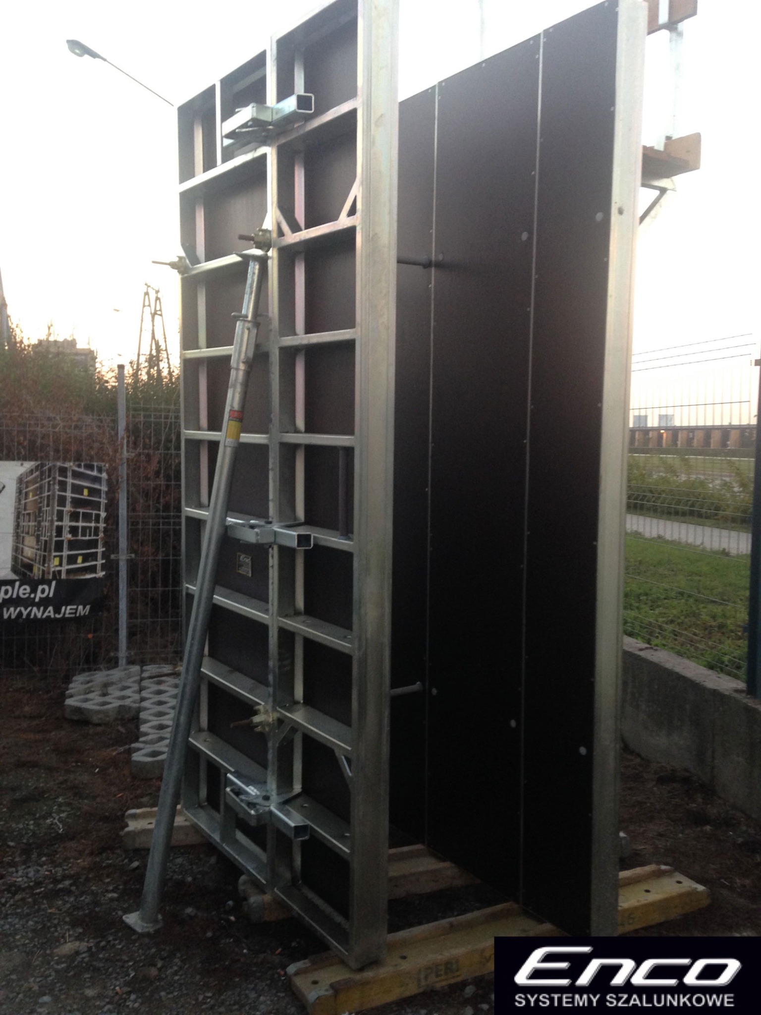 Metalowy system szalunkowy ENCO60 z czarną płytą, podparty teleskopową podporą, ustawiony na placu budowy z widocznym ogrodzeniem i zielenią w tle.