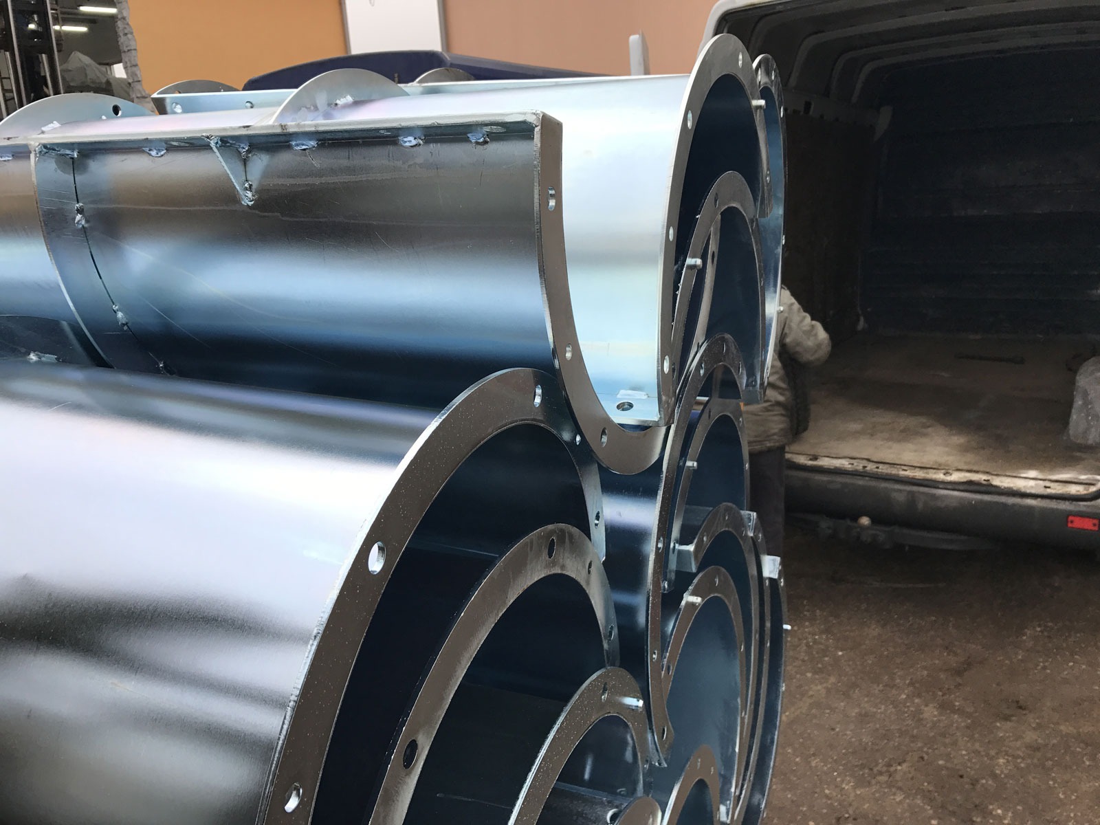 Stos ocynkowanych, okrągłych słupów ENCO z kołnierzami, przygotowanych do transportu w przestrzeni ładunkowej furgonetki.