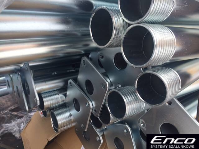 Stos ocynkowanych stempli budowlanych ENCO z gwintowanymi końcówkami i kwadratowymi podstawami, widoczne logo producenta w prawym dolnym rogu.