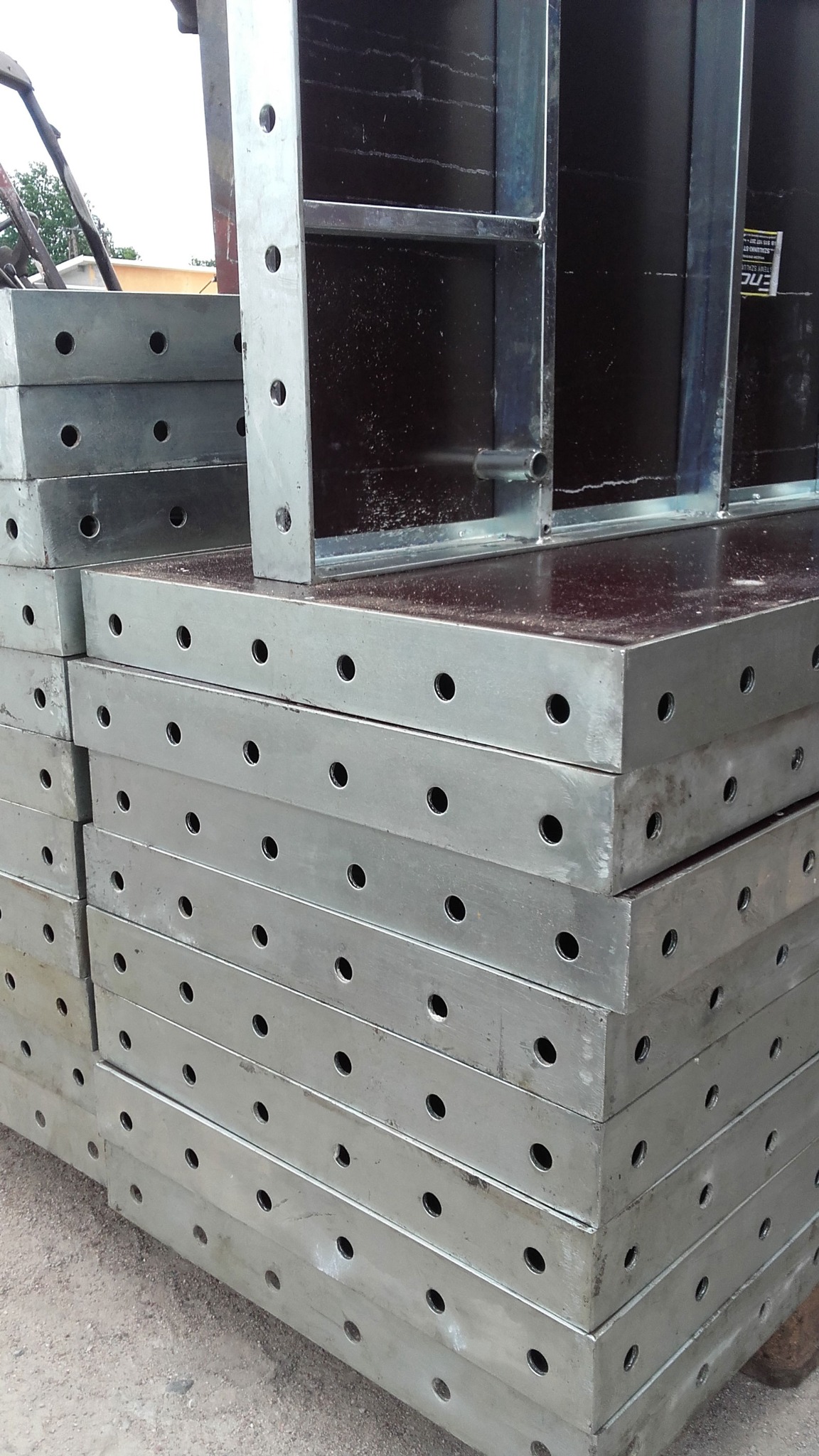 Stos metalowych szalunków systemowych ENCO36 z otworami, ułożonych jeden na drugim, widoczne elementy konstrukcyjne i brązowa płyta szalunkowa.