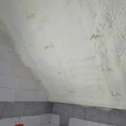 Poddasze ocieplone pianką poliuretanową, widoczne elementy mocujące, ściany z bloczków betonowych z instalacją elektryczną w tle.