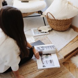 About The Form Weronika Sypuła - Kobieta przegląda katalog z projektami wnętrz na podłodze z próbkami materiałów i dekoracjami w stylu boho.