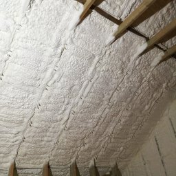 PC PUR Paweł Czerwiak - Poddasze z drewnianą konstrukcją wypełnione białą pianką PUR, widok z dołu, ukazujący strukturę ocieplenia i szczelne wypełnienie przestrzeni.