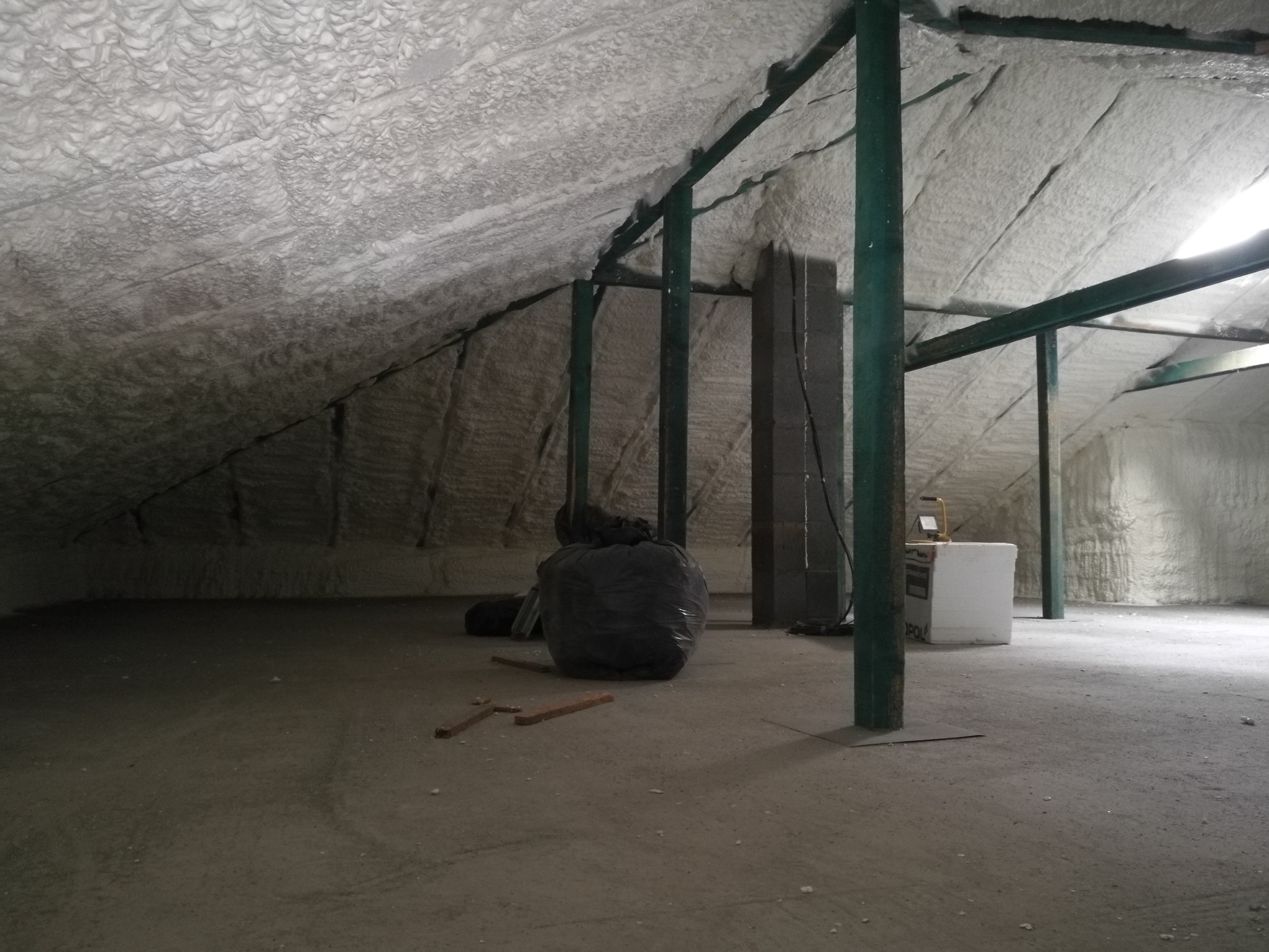 Poddasze po ociepleniu pianką PUR z widoczną konstrukcją nośną i workiem na odpady po prawej stronie. Widoczne ślady piany na podłodze.