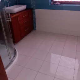 Wykończona łazienka z białą umywalką nablatową na brązowej szafce, kabina prysznicowa z zaokrąglonymi szybami i jasne płytki podłogowe.