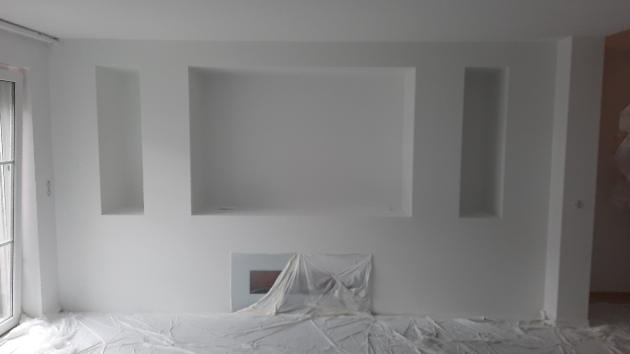 Przygotowane do malowania wnętrze z wnękami w ścianie, zabezpieczone folią malarską.