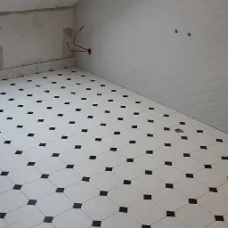 Nowa podłoga z płytek w biało-czarną szachownicę w łazience w Gdańsku, widoczne niedokończone ściany i wystające kable.