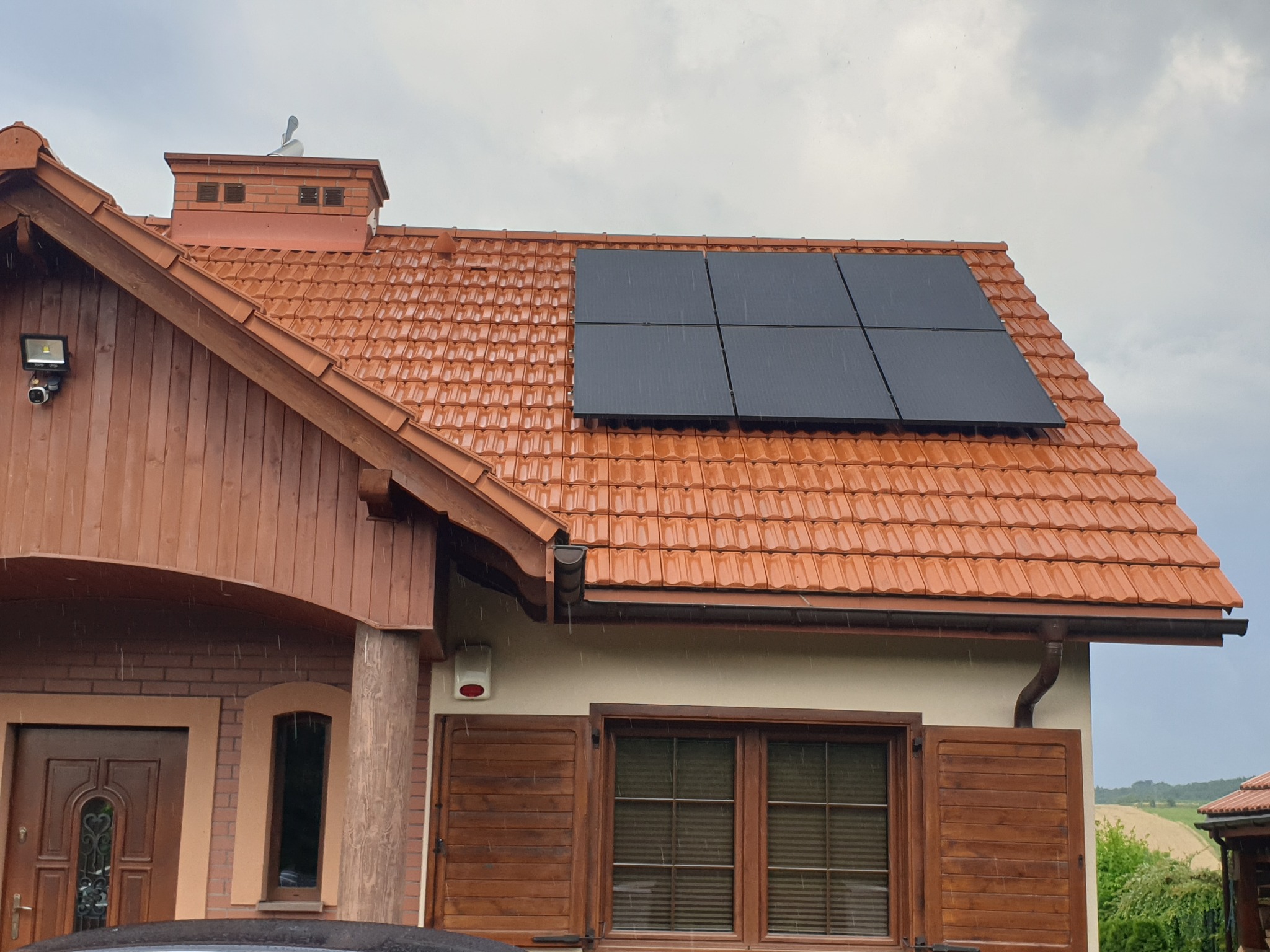 Czerwony dach z ceramicznej dachówki z zamontowanymi czterema panelami fotowoltaicznymi w deszczowy dzień.