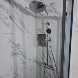 RMB Wnętrza Rafał Borowski - Nowoczesna kabina prysznicowa z chromowaną armaturą i deszczownicą na tle białych płytek imitujących marmur, z wnęką w ścianie.