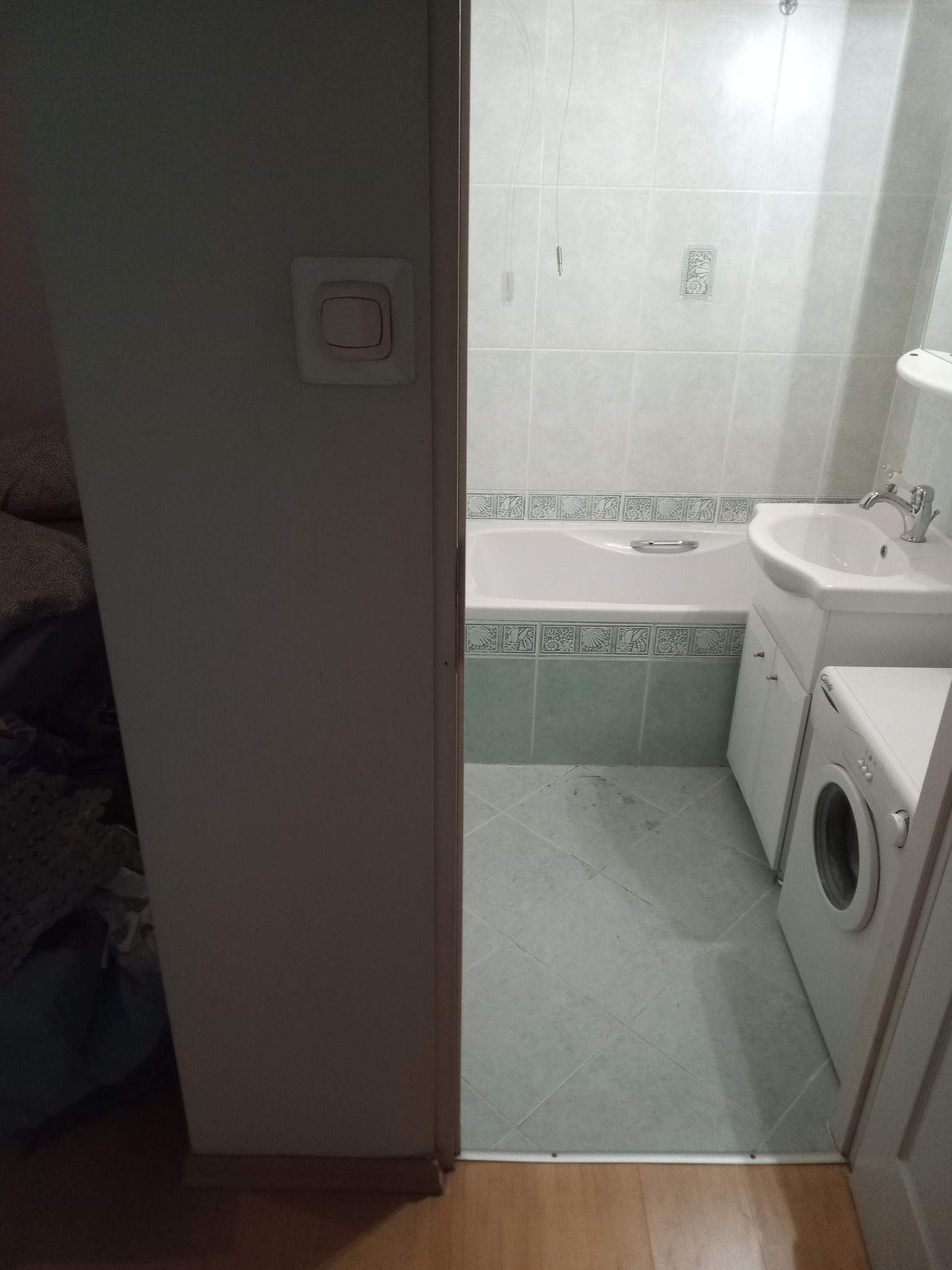 Widok na wyremontowaną łazienkę z wanną obudowaną płytkami z dekoracyjnym wzorem, umywalką z szafką i pralką, widzianą zza uchylonych drzwi.