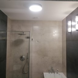 DAABAU Usługi Budowlane Remontowo - Wykończeniowe - Nowoczesna łazienka z kabiną prysznicową typu walk-in, wykończona płytkami w odcieniach szarości i beżu, z chromowaną armaturą i oświetleniem punktowym.