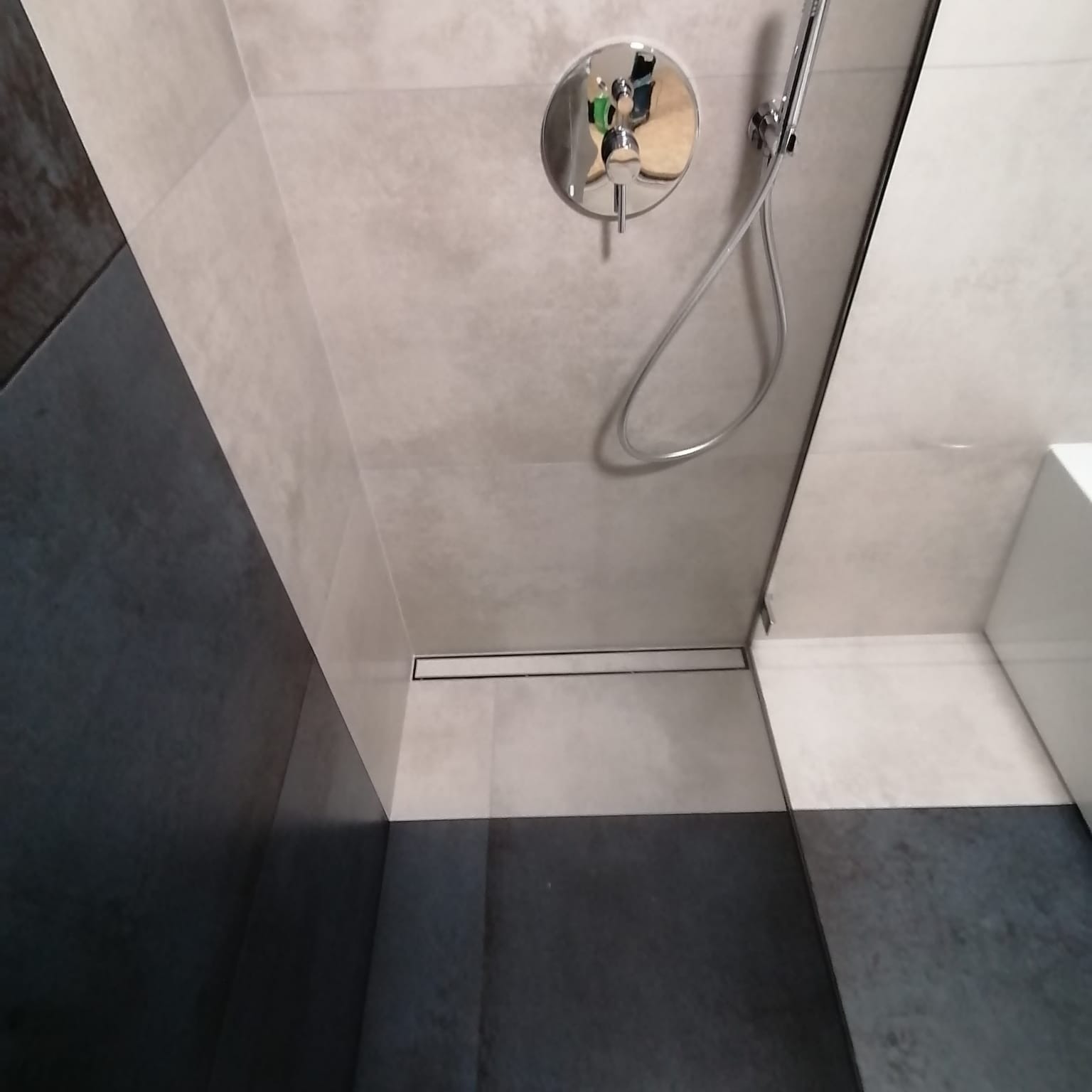Nowoczesna kabina prysznicowa z odpływem liniowym, wykończona szarymi i czarnymi płytkami, widoczna bateria natryskowa z deszczownicą.