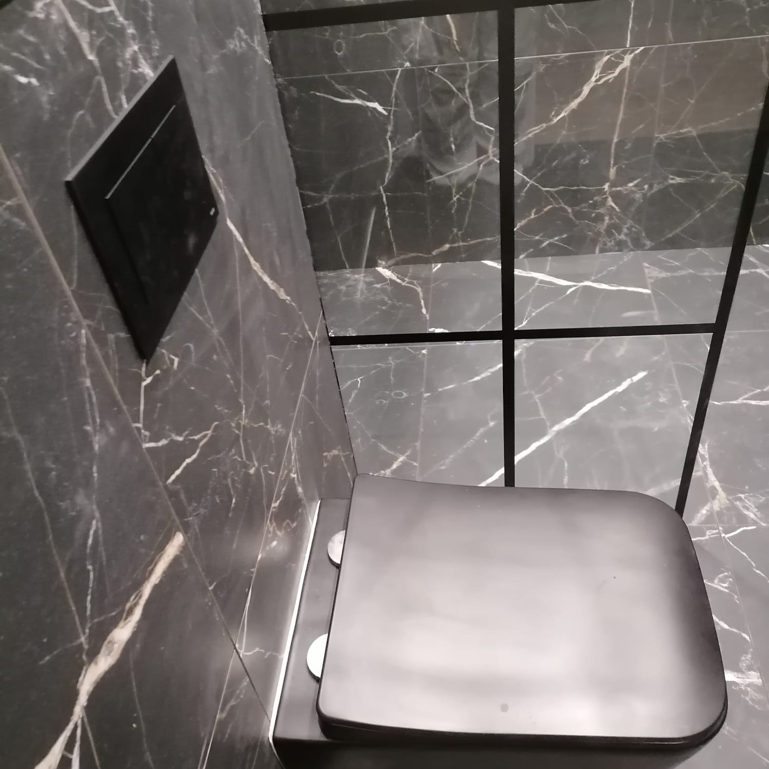 Czarna toaleta z deską wolnoopadającą w nowoczesnej łazience wykończonej płytkami imitującymi czarny marmur z białym żyłkowaniem.