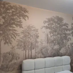 Ściana z tapetą w stylu retro, przedstawiającą leśny krajobraz w odcieniach sepii. Tapeta pokrywa całą ścianę nad łóżkiem z jasnym zagłówkiem.