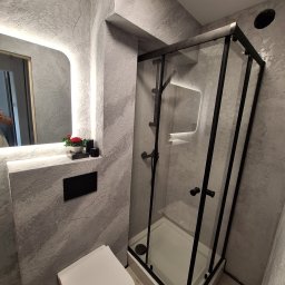 Oktawian Wasiński - Nowoczesna łazienka z kabiną prysznicową typu walk-in, toaletą i lustrem z podświetleniem LED. Ściany pokryte dekoracyjną szarą strukturą. Minimalistyczny design.