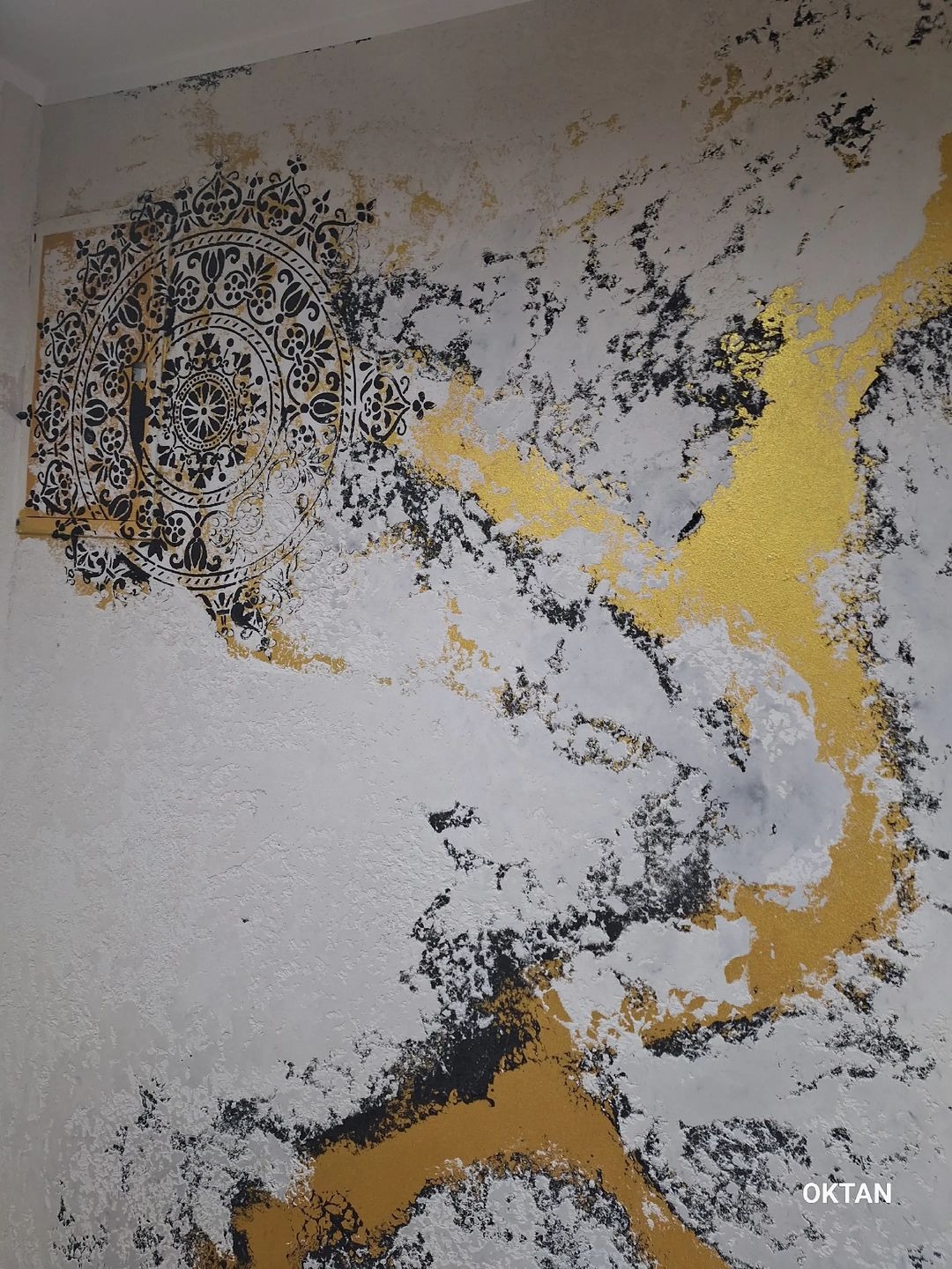 Dekoracyjna ściana z ornamentem mandali w kolorze czarnym i akcentami złota na teksturowanym, jasnym tle.