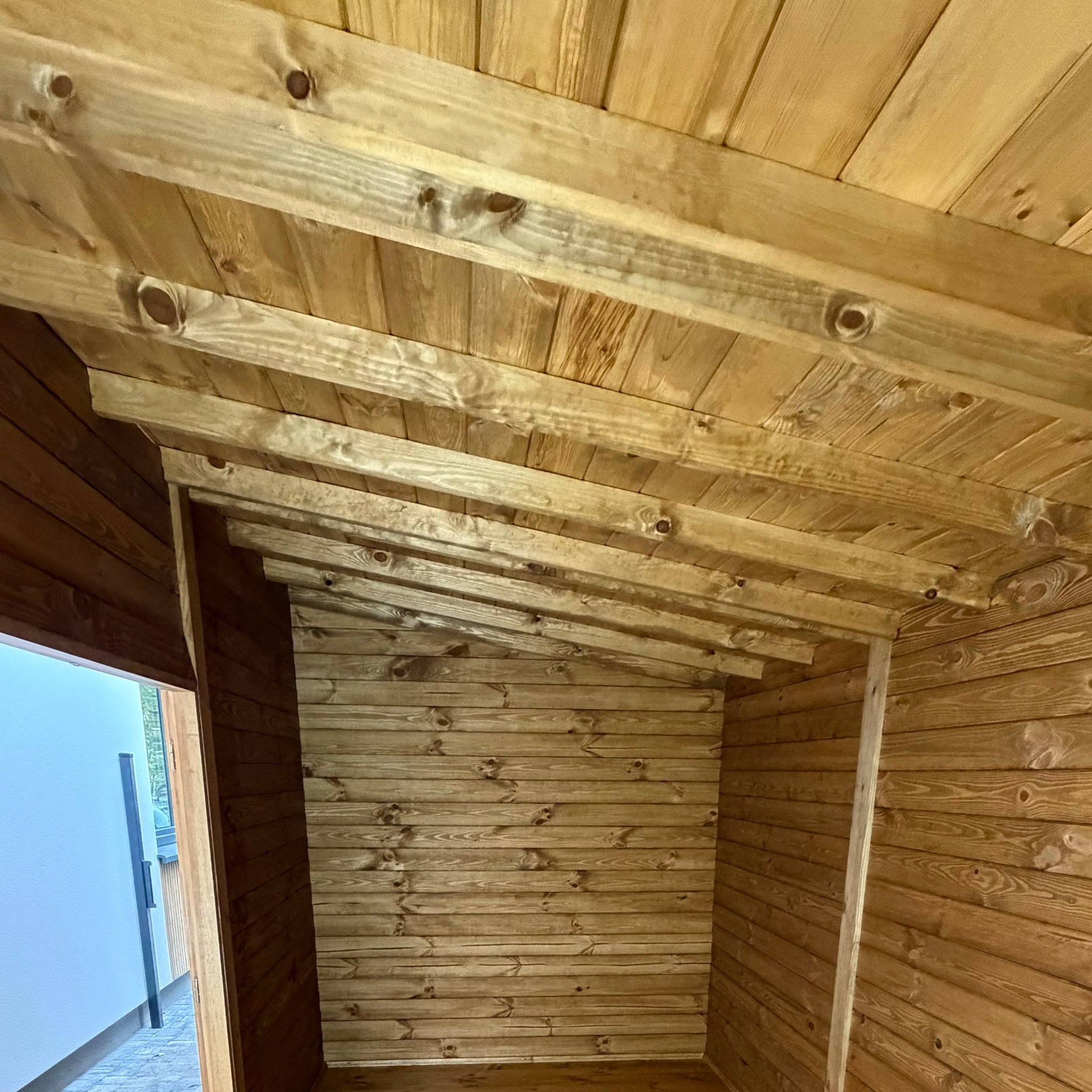 Wnętrze drewnianej konstrukcji w Warszawie, widok z dołu na sufit i ściany z desek. Naturalne drewno, widoczne słoje i sęki. Częściowo otwarty budynek.