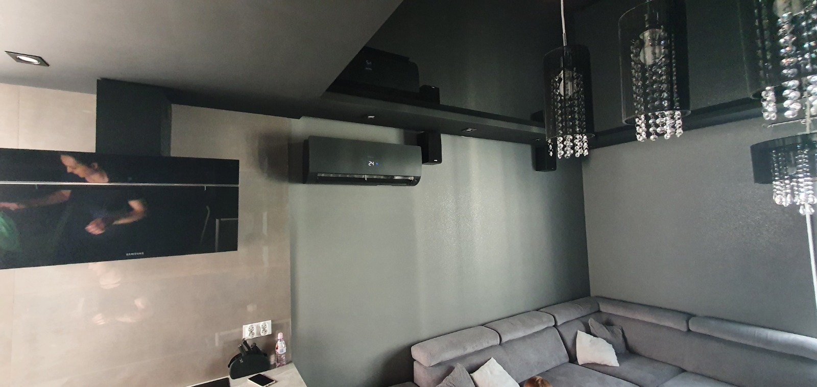 Nowoczesny salon w odcieniach szarości z zamontowanym klimatyzatorem ściennym, widoczne głośniki sufitowe i designerskie lampy wiszące