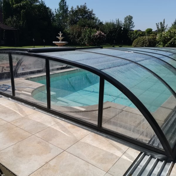 Zadaszony basen ogrodowy z fontanną w tle, widok z poziomu płytek tarasowych.