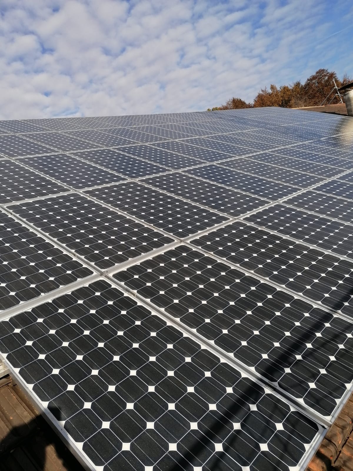 Panele słoneczne zamontowane na brązowym dachu z widocznymi chmurami na niebie w słoneczny dzień.