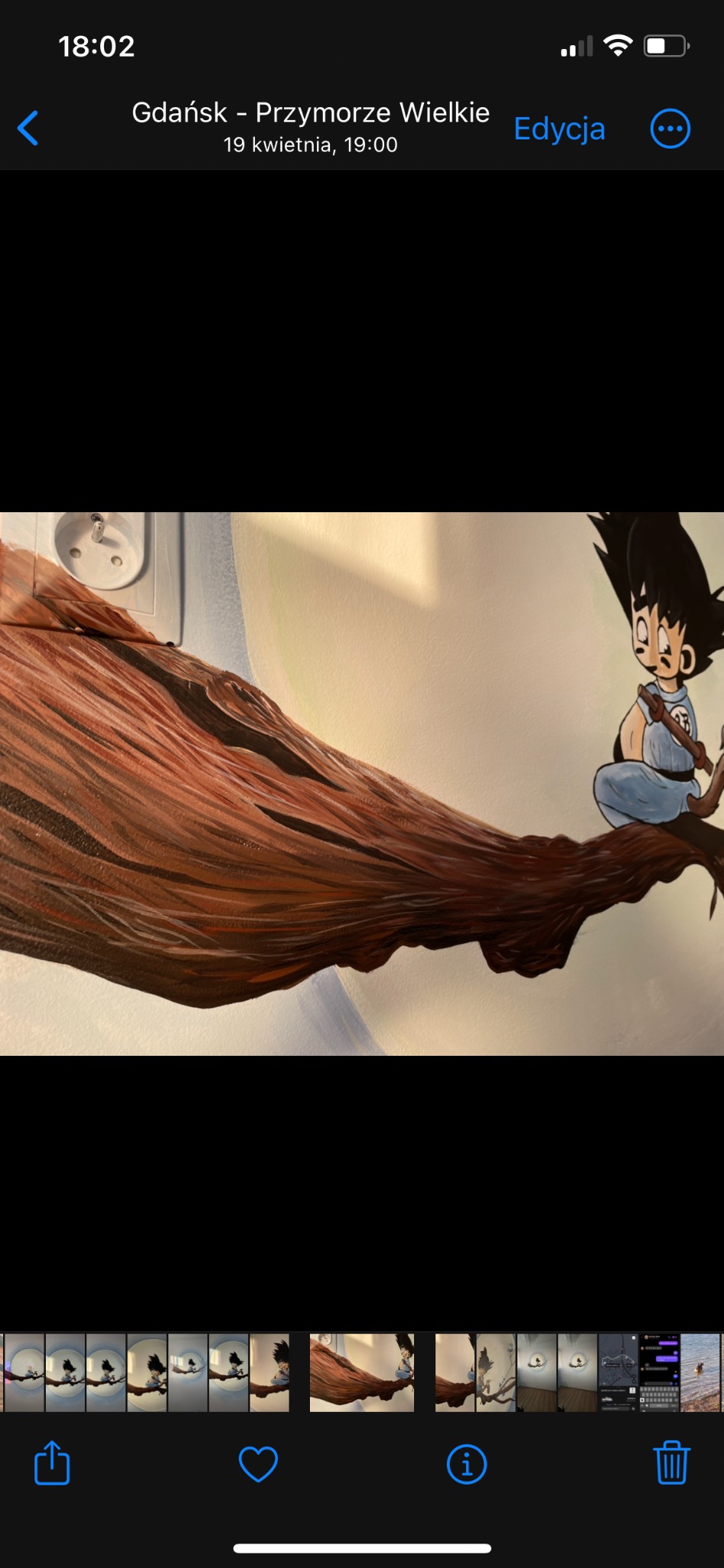 Ręcznie malowana ściana z postacią z kreskówki siedzącą na brązowej gałęzi drzewa, widoczny kontakt elektryczny w górnym rogu.