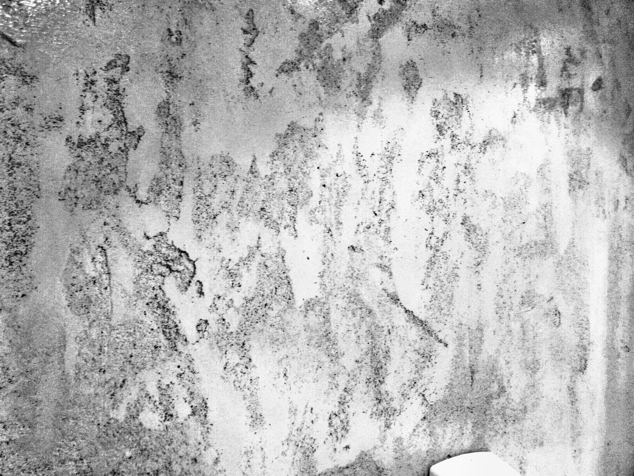 Czarno-białe zdjęcie ściany z odpryskami farby i widocznymi śladami wilgoci, ukazujące stan przed malowaniem.