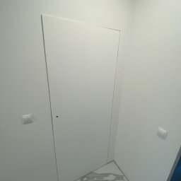 DexoBau Karwowski Damian - Biała, ukryta w ścianie klapa rewizyjna w łazience z marmurową posadzką i włącznikami światła po bokach.