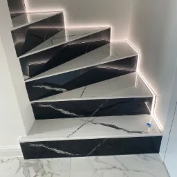 Schody wykończone czarno-białym marmurem z podświetleniem LED na krawędziach stopni i wzdłuż ściany, widok z dołu, fragment marmurowej podłogi.