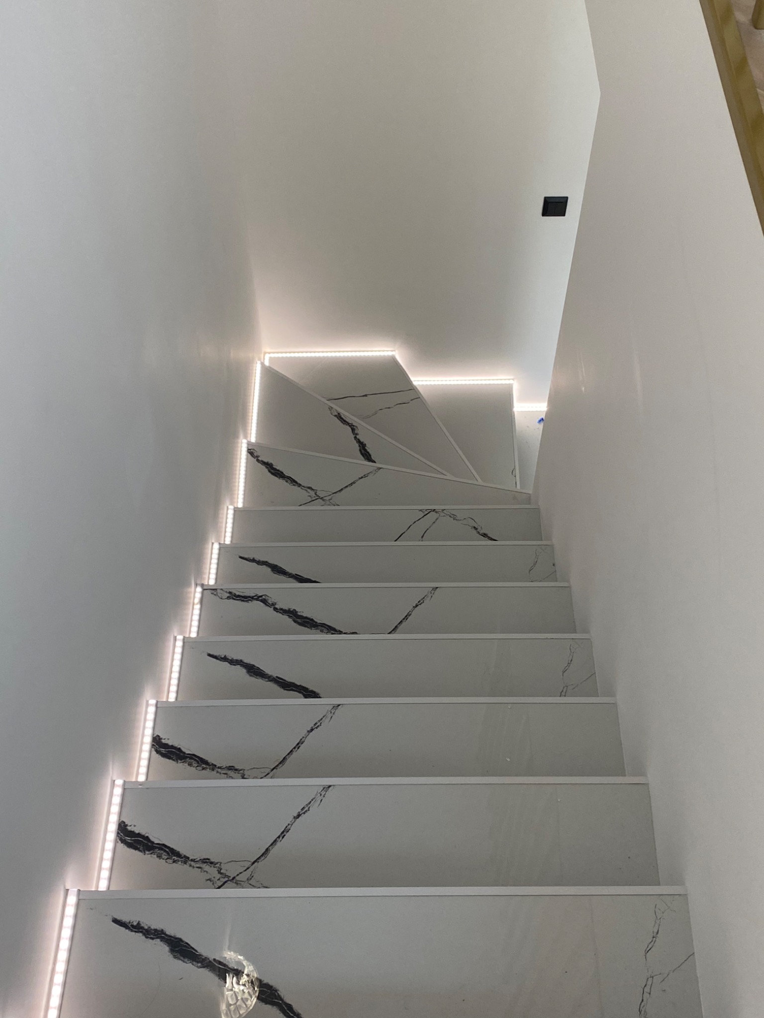 Schody wykończone białym marmurem z czarnymi żyłkami, podświetlone taśmą LED po bokach, widok z dołu.