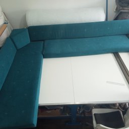 AFDOR - Turkusowy narożnik w trakcie tworzenia, widoczne szpilki na materiale. Narożnik częściowo ułożony na białym stole, w tle materiały i narzędzia tapicerskie.