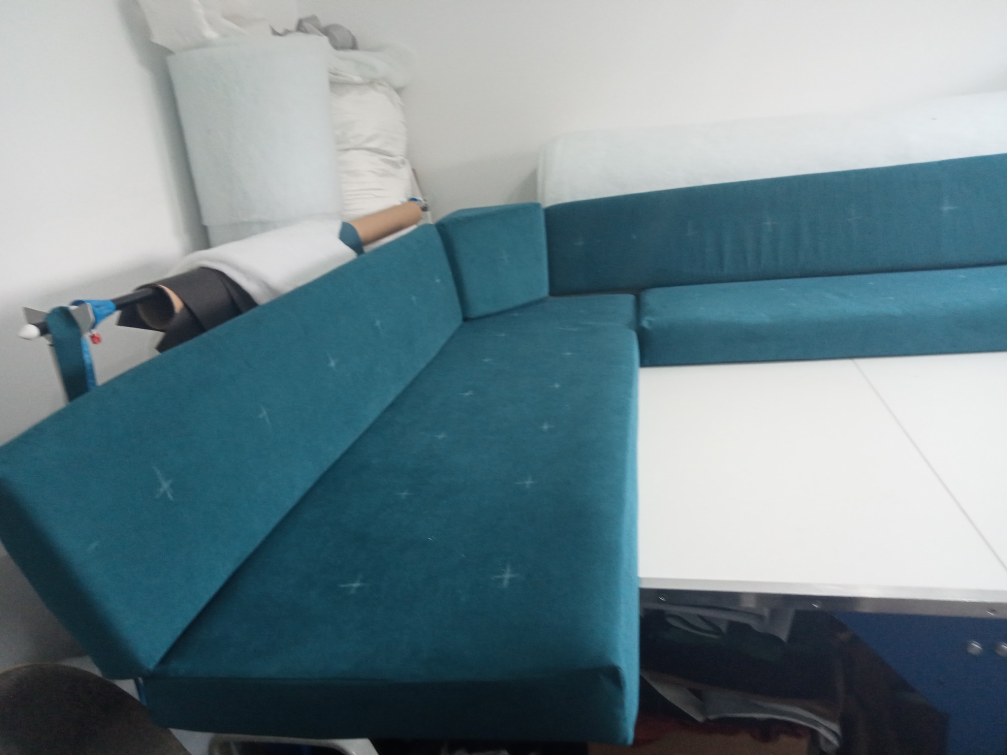 Turkusowy narożnik z widocznymi znakami krawieckimi leży na stole w pracowni tapicerskiej, w tle materiały i narzędzia. Widok z góry.