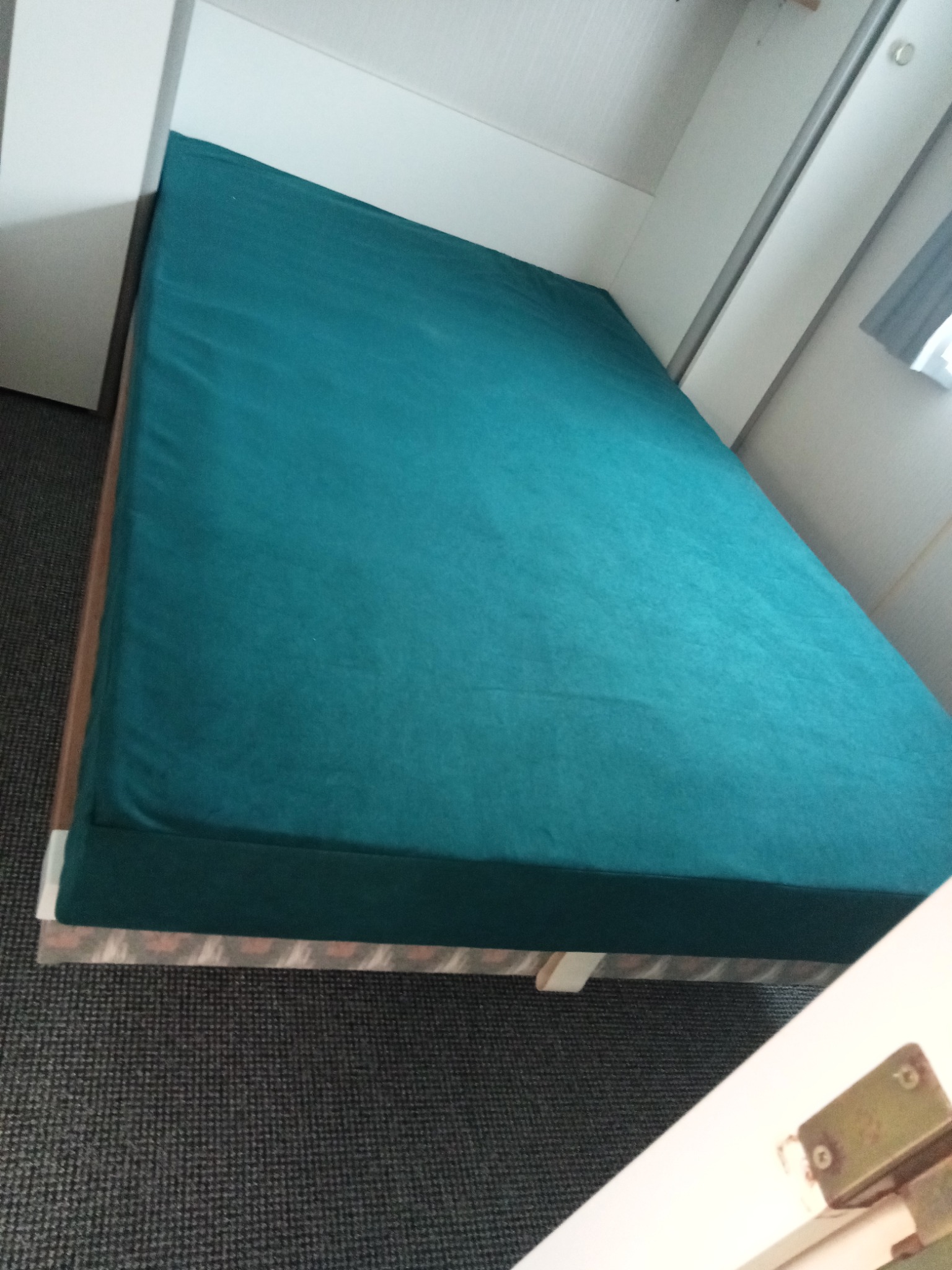 Turkusowy materac na łóżku z białym zagłówkiem, widok z góry. Ciemna wykładzina podłogowa. Minimalistyczny design sypialni.