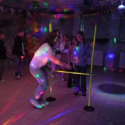 MK'smile Krzysztof Sobik - Dziewczyna w limbo pod kolorowymi światłami na imprezie dla dzieci. W tle grupa dzieci i dekoracje, tworzące radosną atmosferę zabawy.