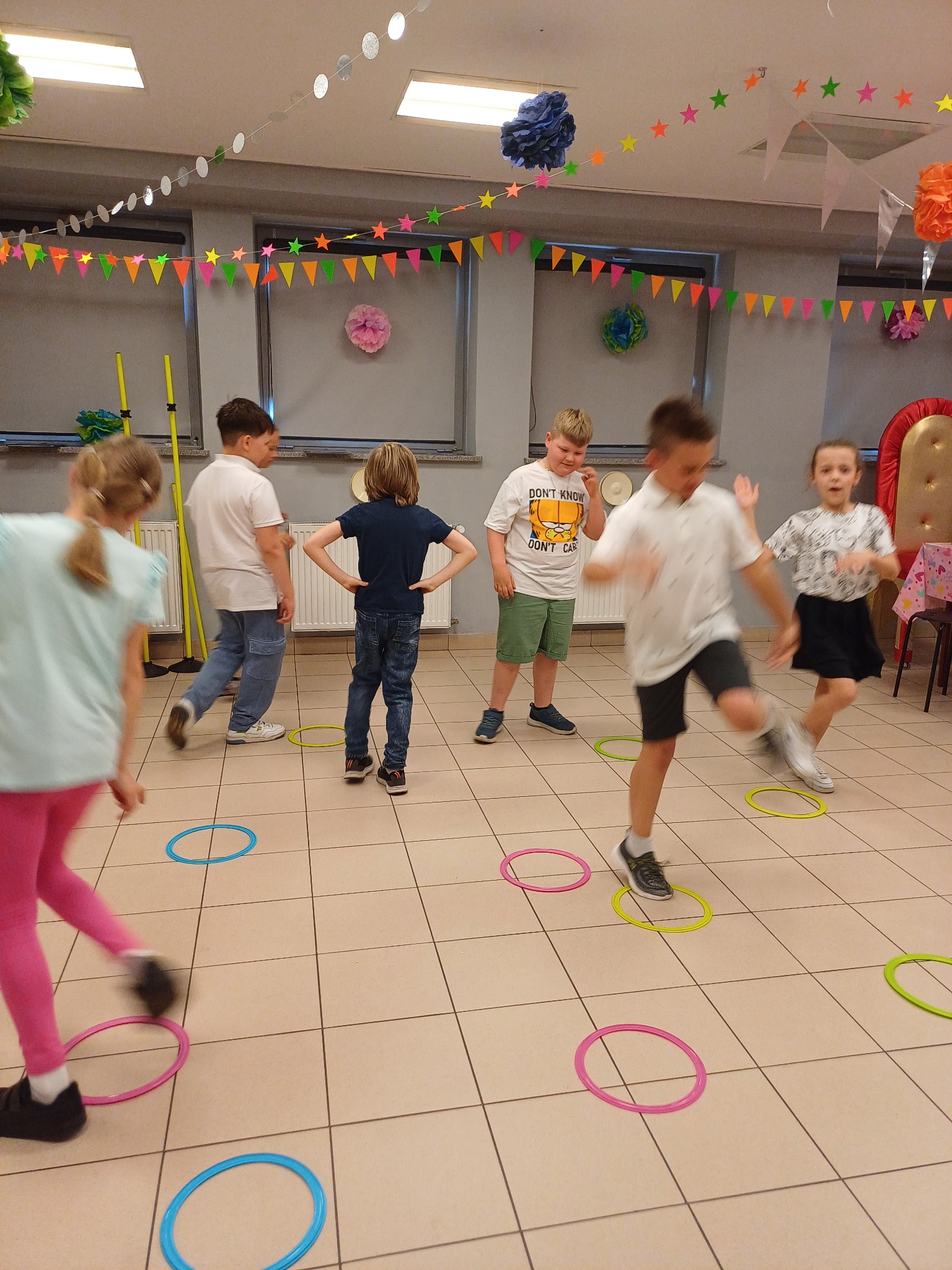 Dzieci podczas zabawy z kolorowymi obręczami na podłodze w udekorowanym pomieszczeniu. Dekoracje wiszą na ścianach i suficie. Aktywna rozrywka dla dzieci.