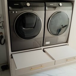 Stablo Meble - Szaro-beżowa zabudowa z pralką i suszarką Samsung, szuflady z poziomymi, złotymi uchwytami, marmurowa podłoga.