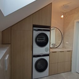 Stablo Meble - Funkcjonalna zabudowa łazienki na poddaszu w Szczecinie. Jasne drewno, pralka i suszarka w kolumnie, umywalka z szafkami, okrągłe lustro. Wykorzystanie przestrzeni.