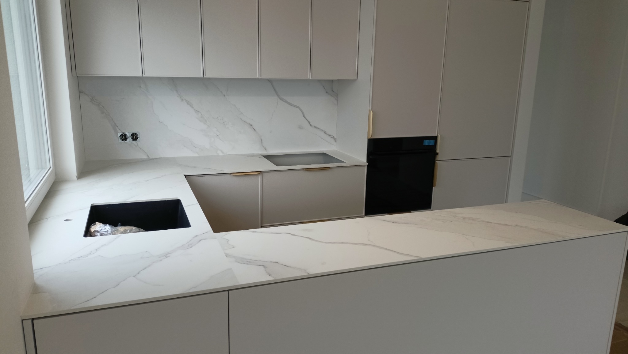 Jasna kuchnia z marmurowym blatem i złotymi uchwytami. Nowoczesny design z wyspą kuchenną i wbudowanym sprzętem AGD. Minimalistyczne szafki wiszące i podłogowe.