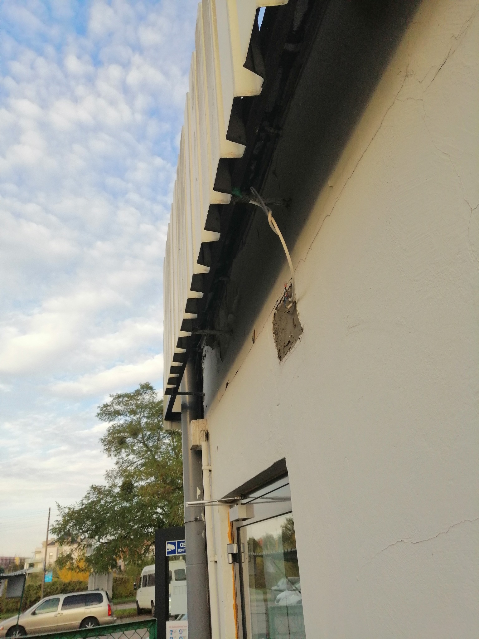 Elewacja budynku w Toruniu z widocznym uszkodzeniem tynku i wystającymi przewodami elektrycznymi, przygotowana do naprawy.