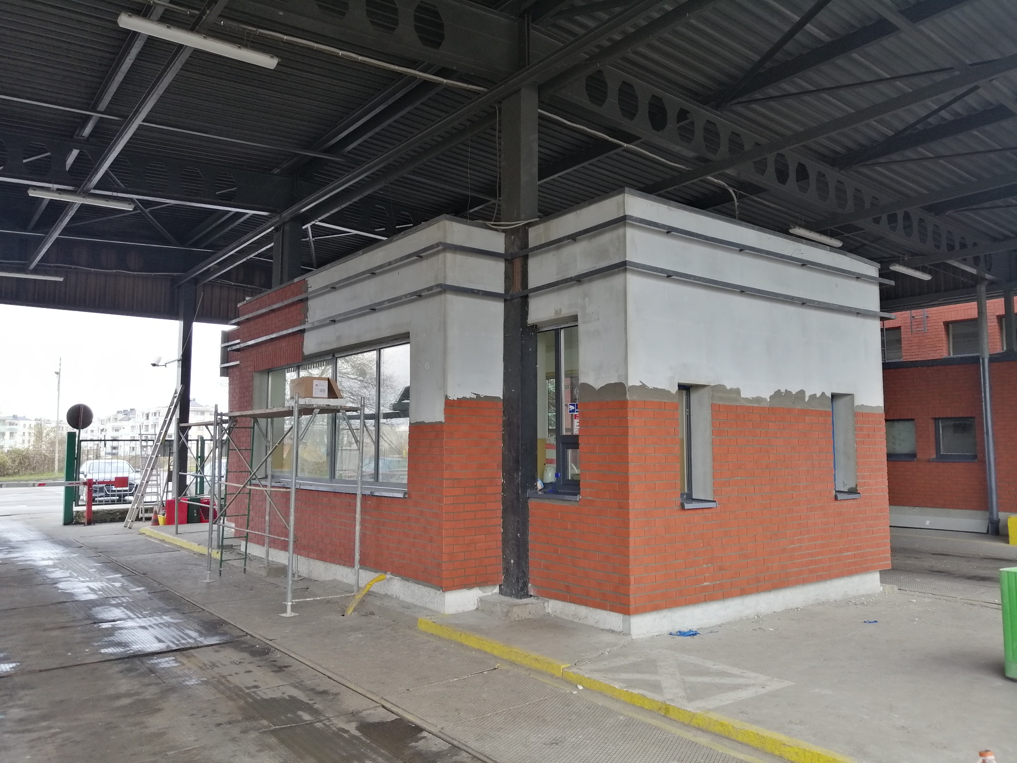 Budynek z cegły i betonu pod zadaszeniem, częściowo otynkowany, z rusztowaniem i drabiną, w trakcie prac wykończeniowych.