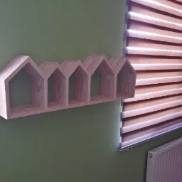 Półka ścienna w kształcie rzędu domków z jasnego drewna, przymocowana do zielonej ściany obok okna z żaluzjami poziomymi.