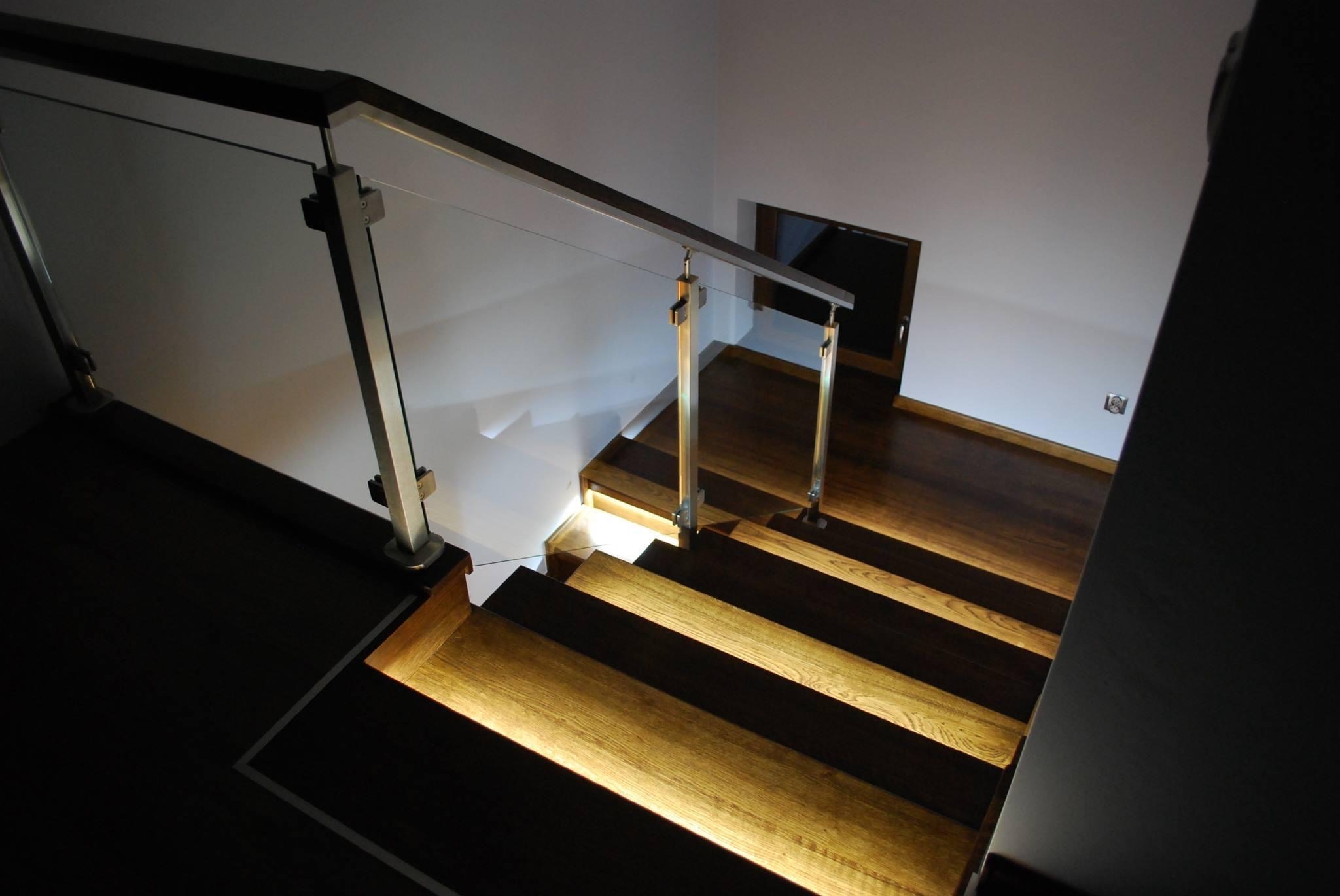 Nowoczesne schody z podświetlanymi stopniami, szklaną balustradą i metalowymi elementami, widok z góry.