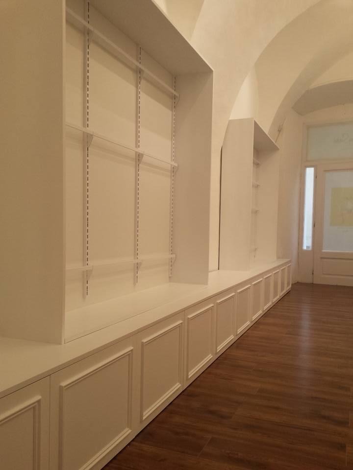 Białe, zabudowane szafy wnękowe z regulowanymi półkami i dolnymi szafkami z dekoracyjnymi panelami, w pomieszczeniu z drewnianą podłogą i łukowatym sufitem.